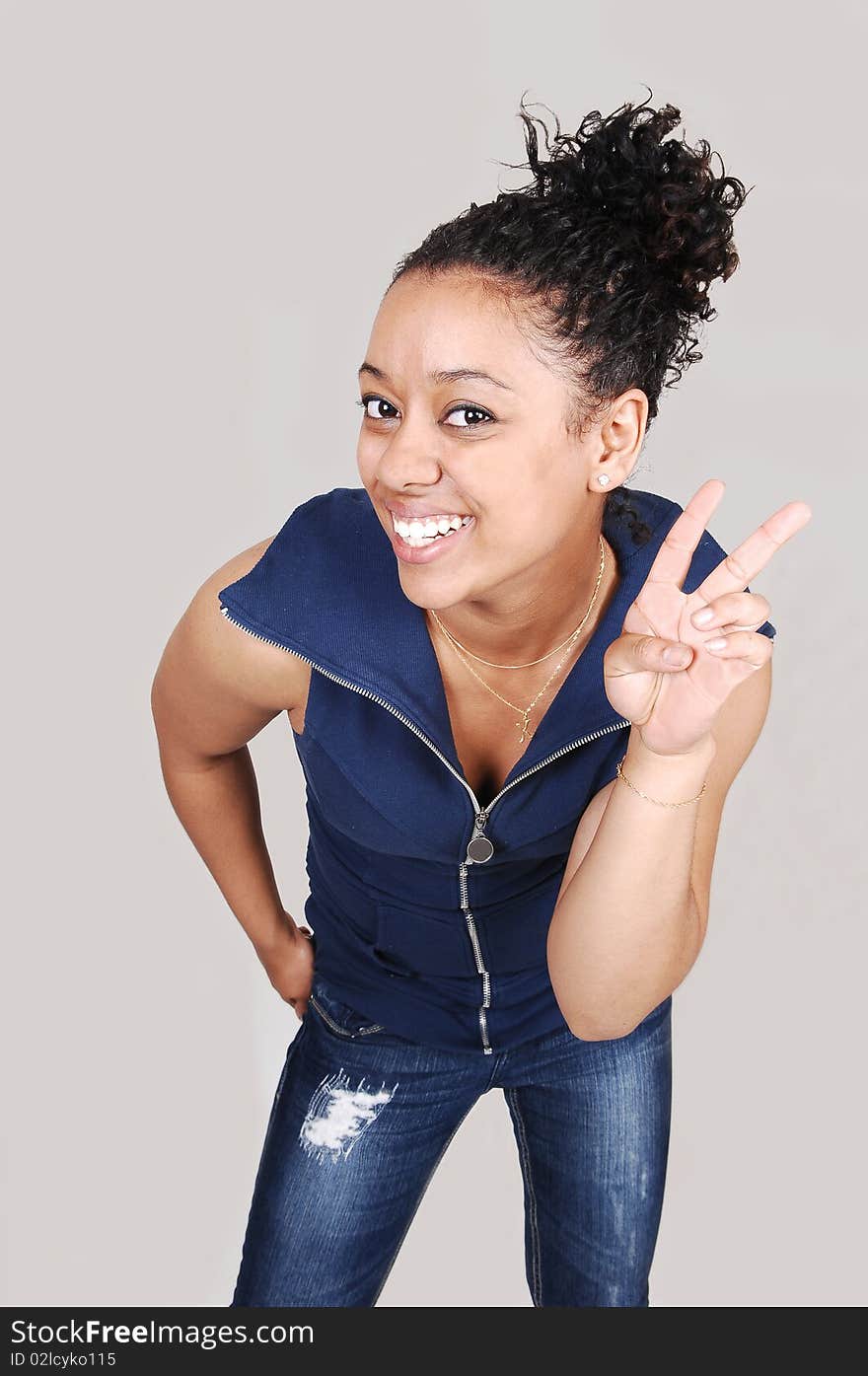 A young, pretty Hispanic woman standing in the studio, smiling and giving signs with her fingers over light gray background. A young, pretty Hispanic woman standing in the studio, smiling and giving signs with her fingers over light gray background.