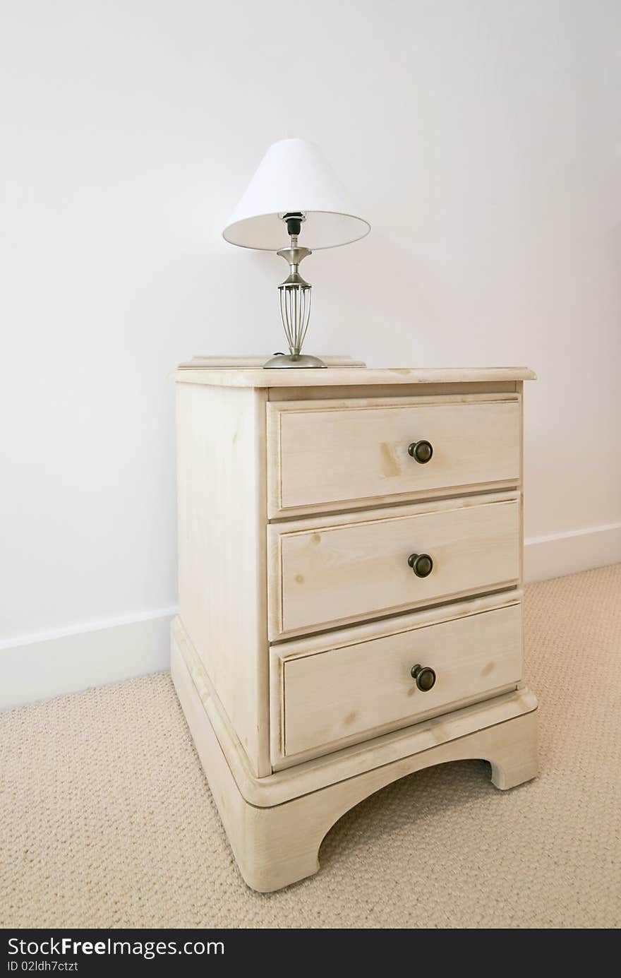 Detail of a wooden bedside table with three drawers and bedside lamp