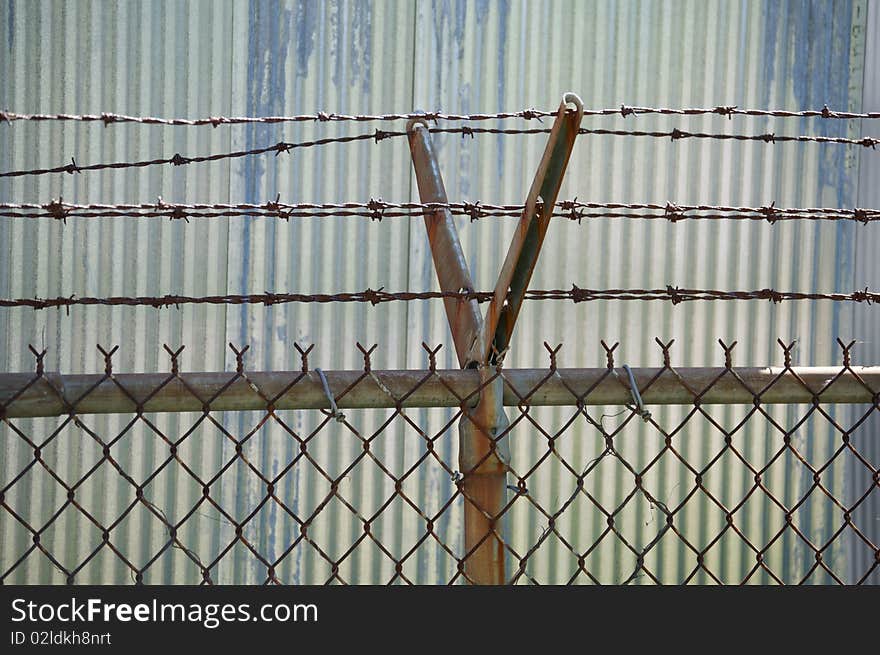 Detail of fencing with barbed wire. Corrugated metal siding in the background.