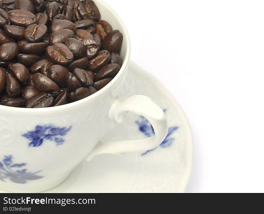 Roasted coffee beans fill china cup and saucer. Roasted coffee beans fill china cup and saucer