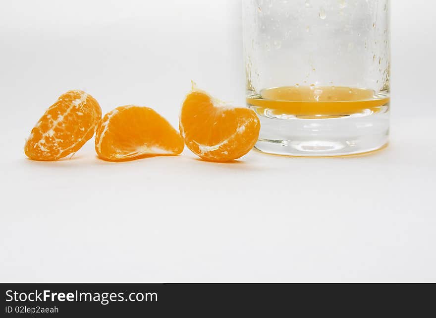 The segments of a tangerine lying near a glass with natural orange juice. The segments of a tangerine lying near a glass with natural orange juice