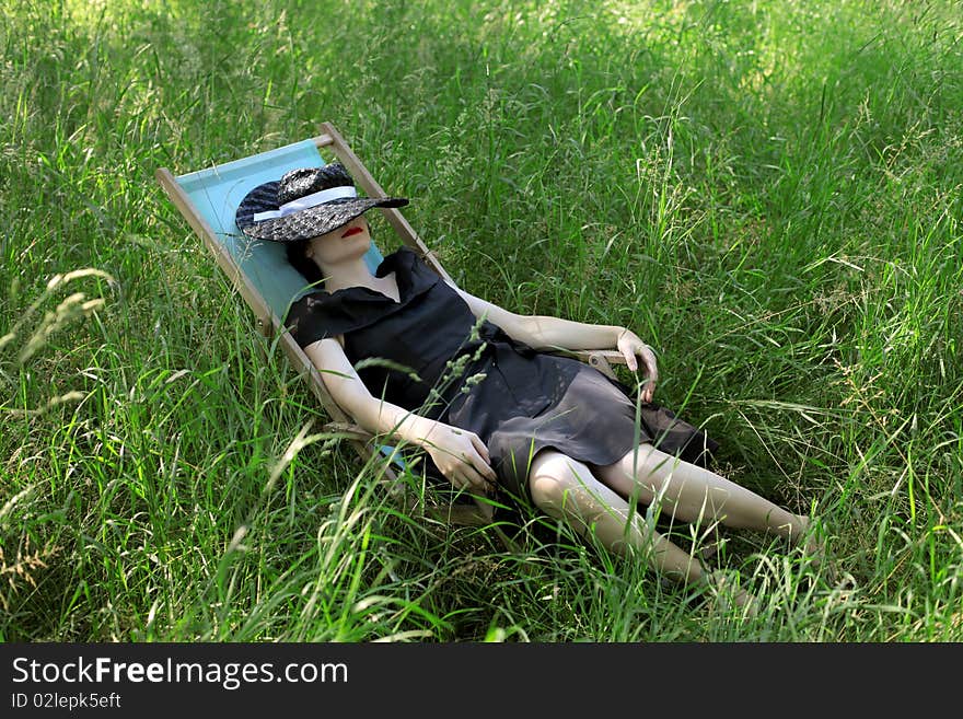 Beautiful elegant woman lying on a deckchair on a green meadow. Beautiful elegant woman lying on a deckchair on a green meadow