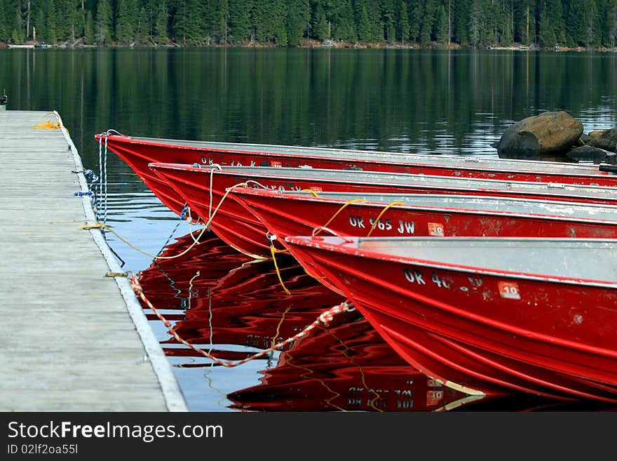 4 red boats tied up at a dock beside each other with pine forest and lake background. 4 red boats tied up at a dock beside each other with pine forest and lake background.