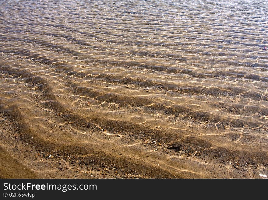 On the beach with ripples on the water surface.