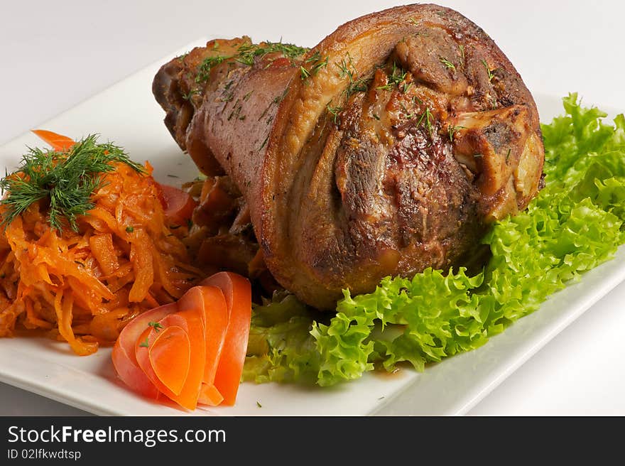 Roast pork leg rests on a plate with garnish, fresh tomatoes and lettuce. Roast pork leg rests on a plate with garnish, fresh tomatoes and lettuce