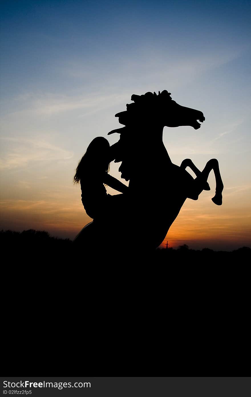 A girl sits on his horse, which reared against the sunset. A girl sits on his horse, which reared against the sunset.