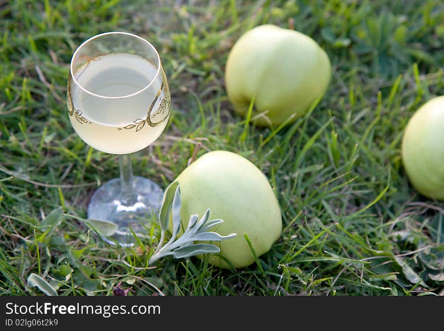 Glass of wine with green apples on the grass