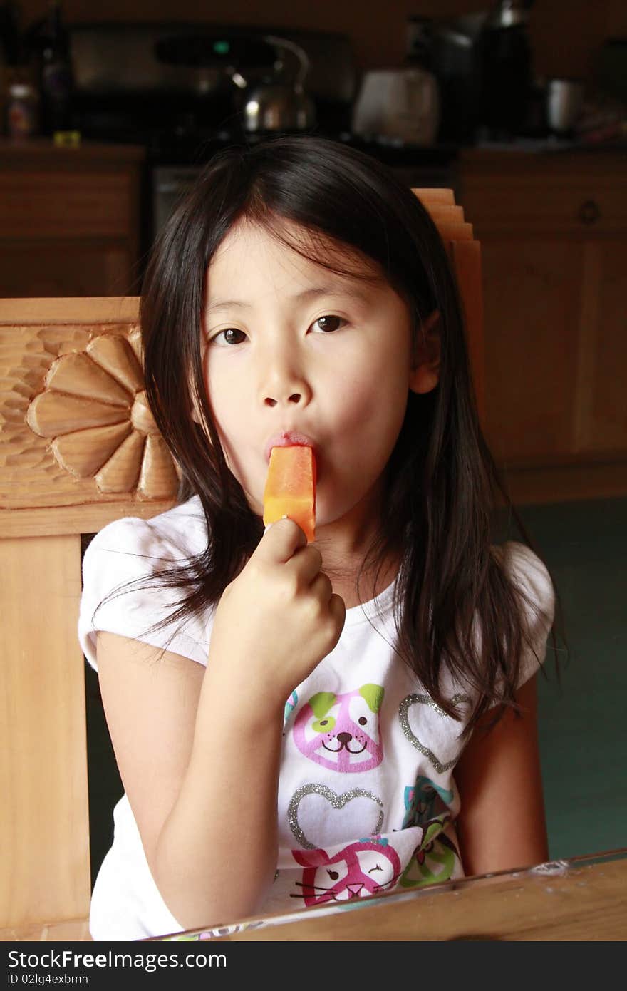 Little asia girl eating an orange ice pop. Little asia girl eating an orange ice pop