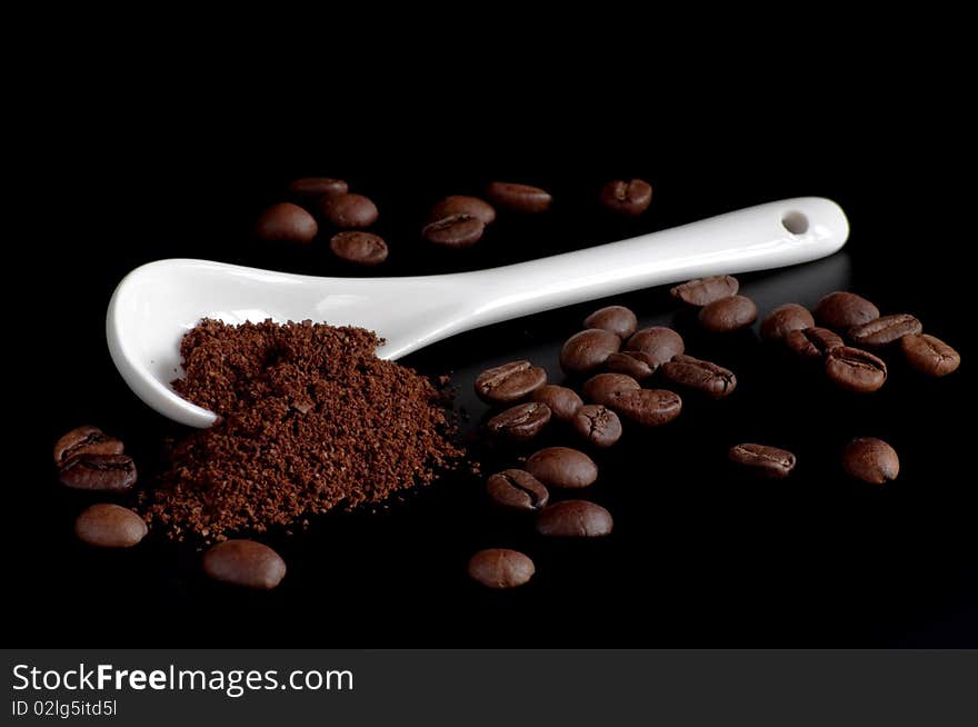 White spoon with coffee powder and beans on a black  background. White spoon with coffee powder and beans on a black  background