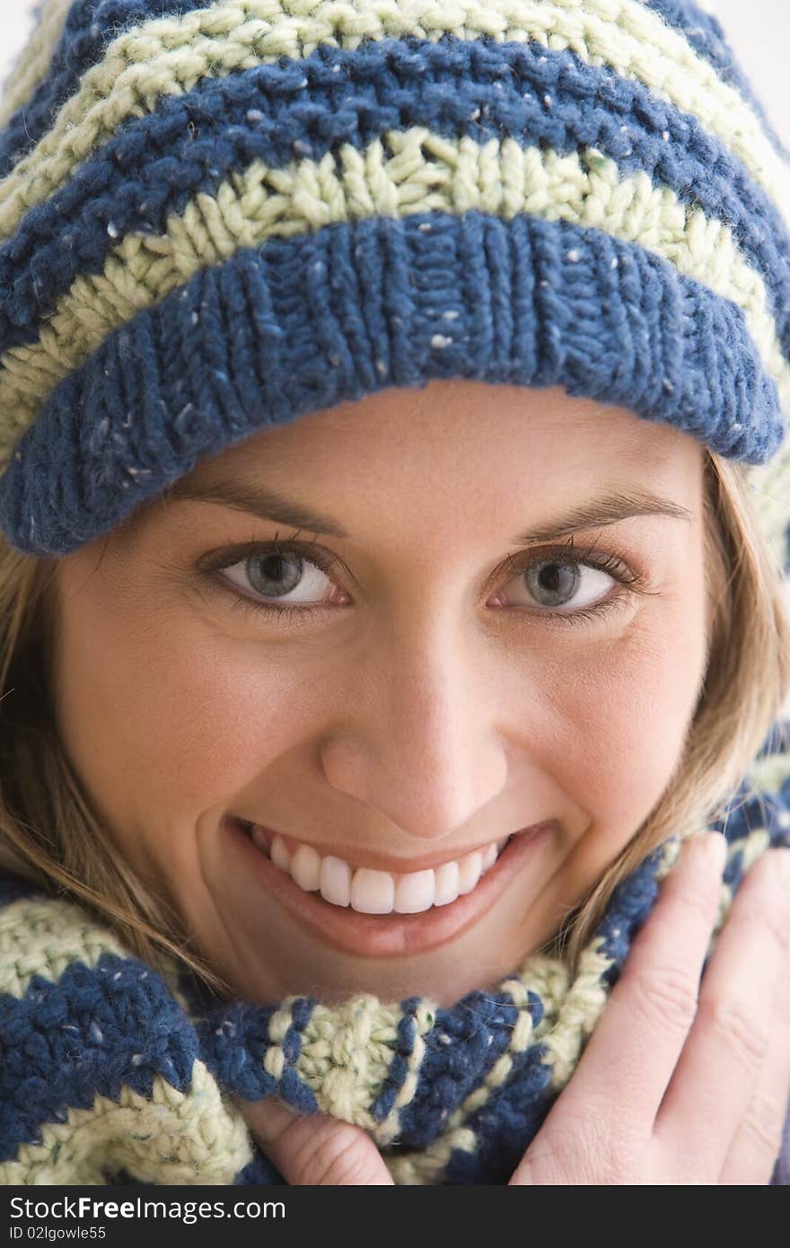 An attractive young woman is smiling and wearing a blue and beige knit cap and scarf. Vertical shot. An attractive young woman is smiling and wearing a blue and beige knit cap and scarf. Vertical shot.