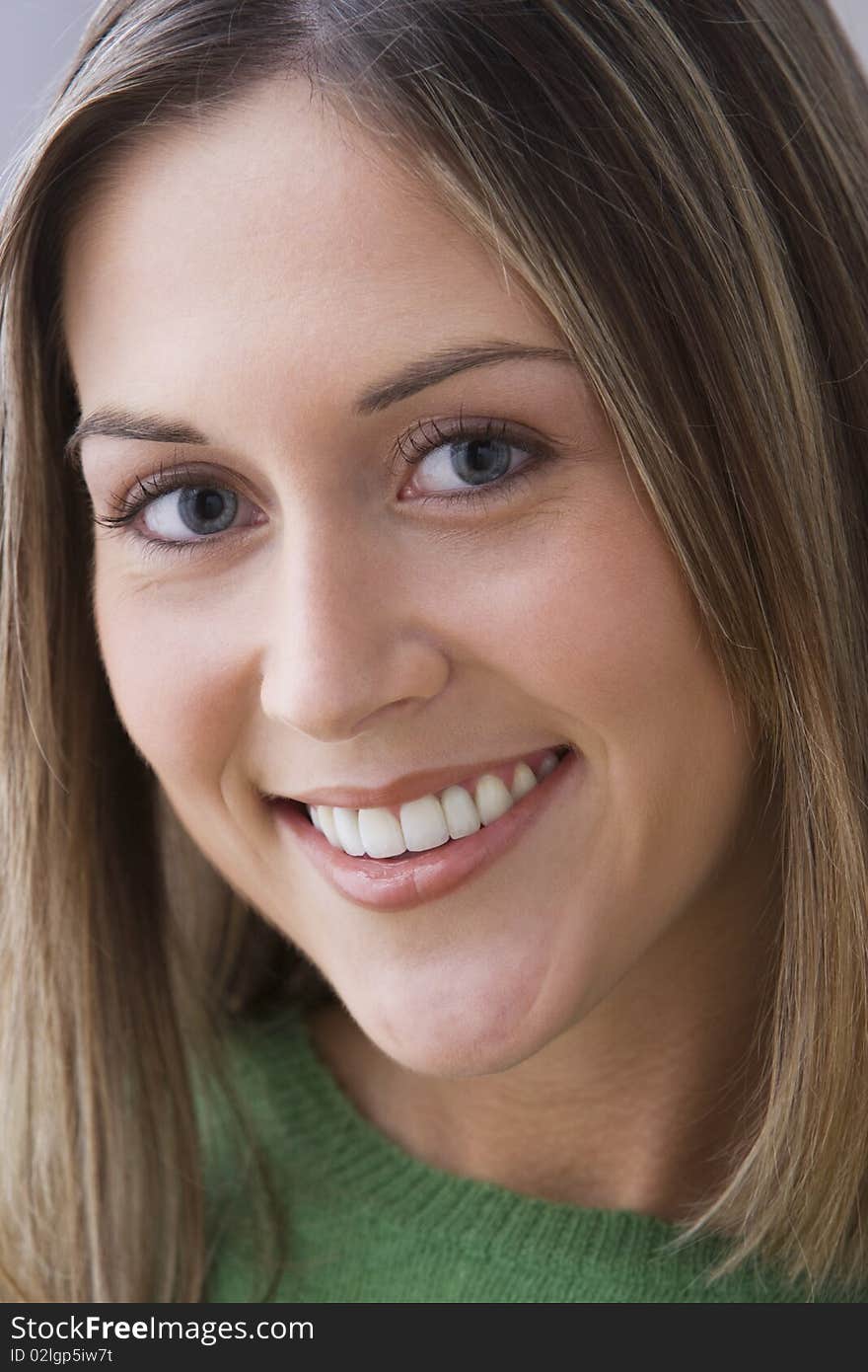 An attractive young woman is wearing a green sweater and smiling at the camera. Vertical shot. An attractive young woman is wearing a green sweater and smiling at the camera. Vertical shot.