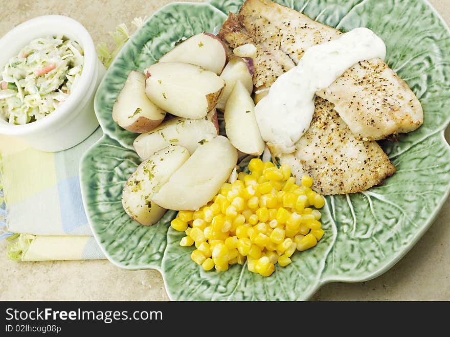 A broiled tilapia dinner with potatoes, corn and coleslaw. A broiled tilapia dinner with potatoes, corn and coleslaw