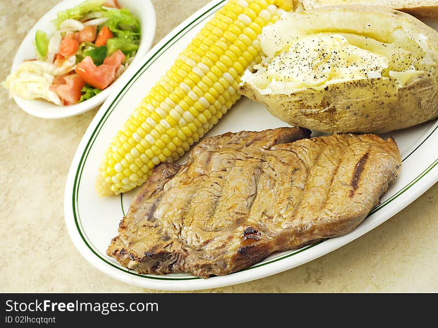 A grilled ribeye steak dinner with corn, baked potato and salad. A grilled ribeye steak dinner with corn, baked potato and salad