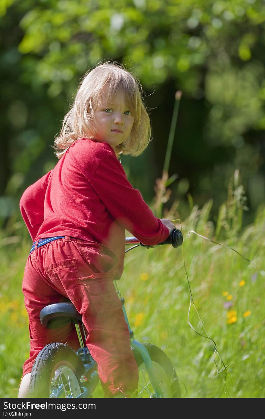 Boy with long blond hair riding a bike in the garden. Boy with long blond hair riding a bike in the garden