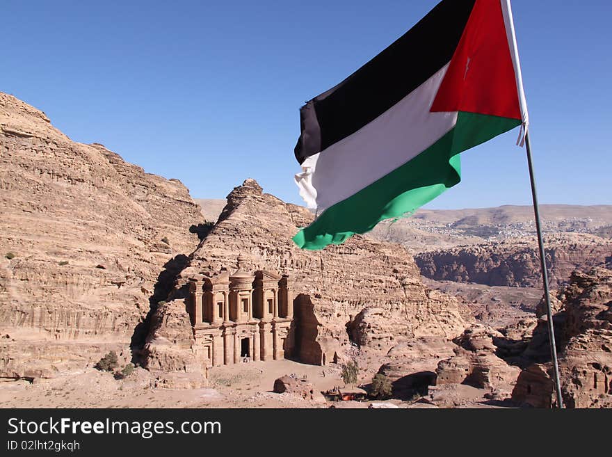 The Monastery, Petra's largest monument, dates from the 1st century BCE. It was dedicated to Obodas I and is believed to be the symposium of Obodas the god. This information is inscribed on the ruins of the Monastery. Here the jordanian flag flapping in front, the Monastery in the background. The Monastery, Petra's largest monument, dates from the 1st century BCE. It was dedicated to Obodas I and is believed to be the symposium of Obodas the god. This information is inscribed on the ruins of the Monastery. Here the jordanian flag flapping in front, the Monastery in the background.