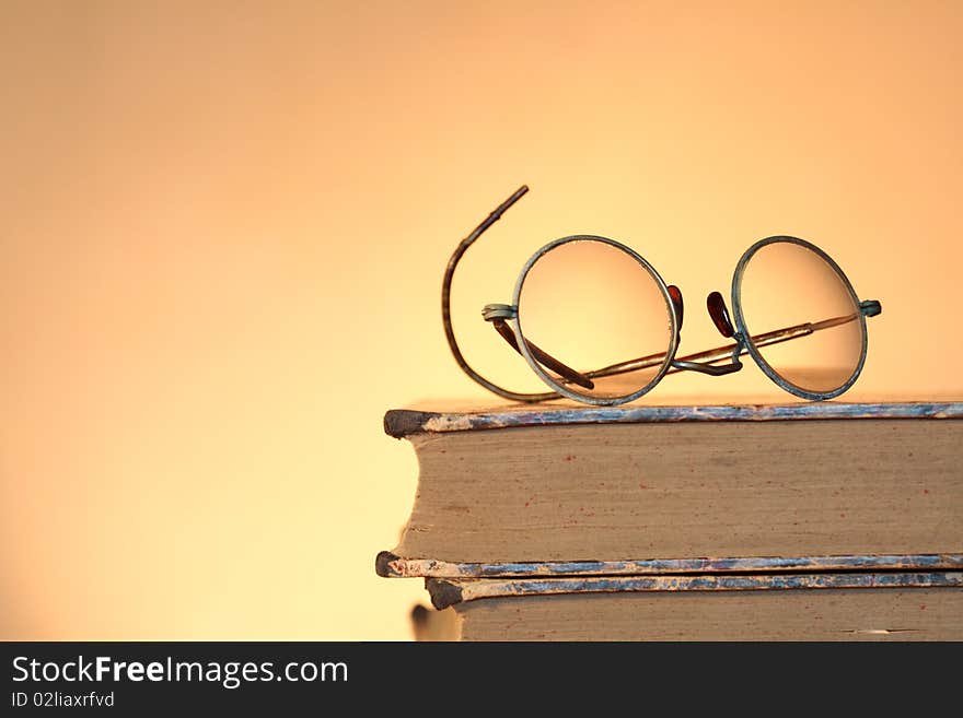 Old spectacles lying on ancient books isolated on yellow background