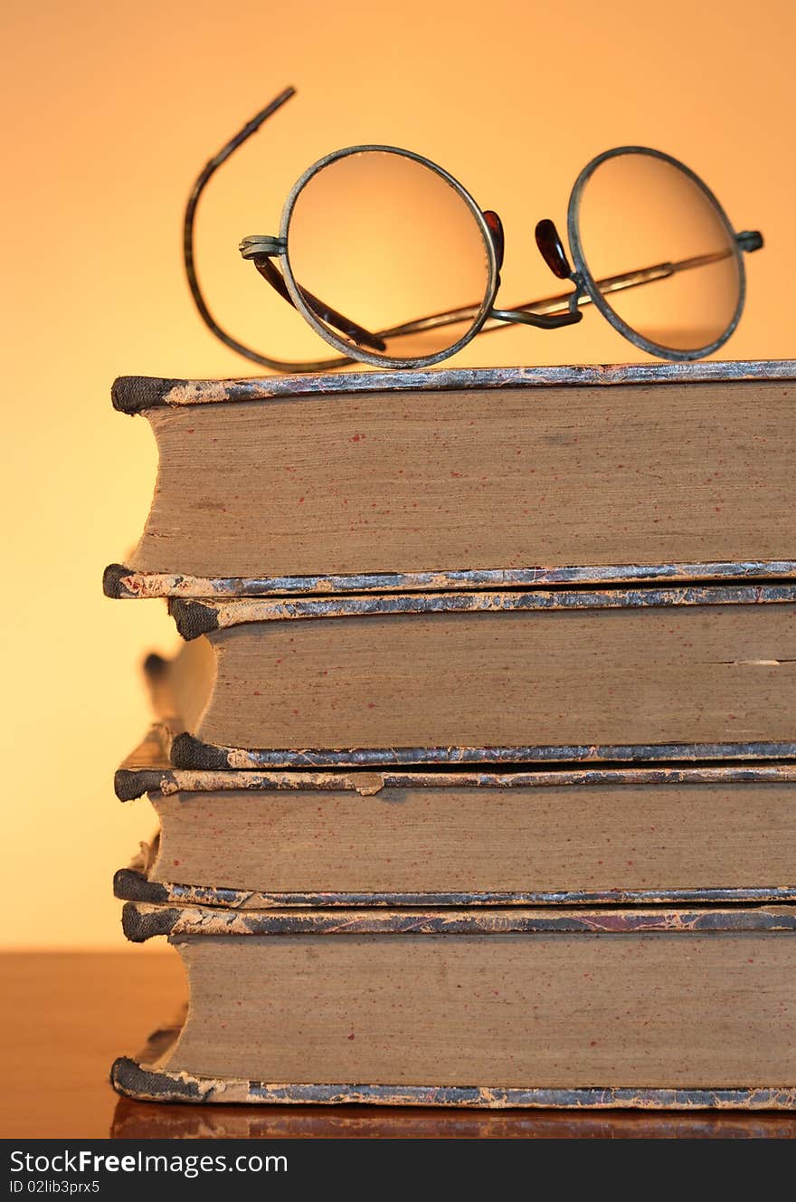 Old spectacles lying on ancient books isolated on yellow background