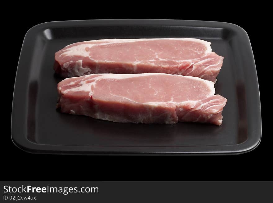 Two raw pork steaks on the dark square plate isolated over black background