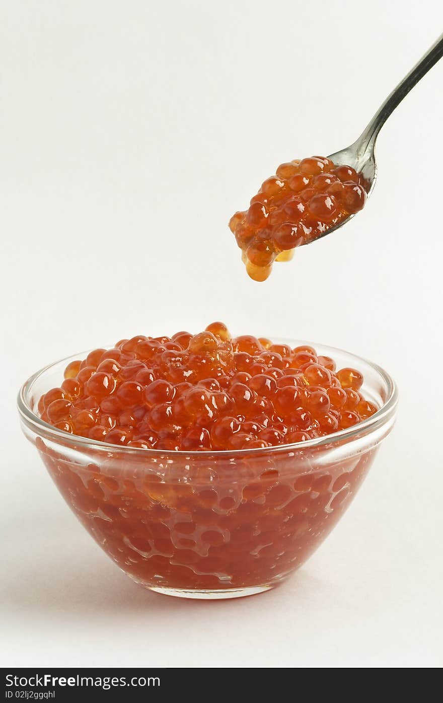 Red caviar in the little glass bow and spoon isolated over grey gradient background