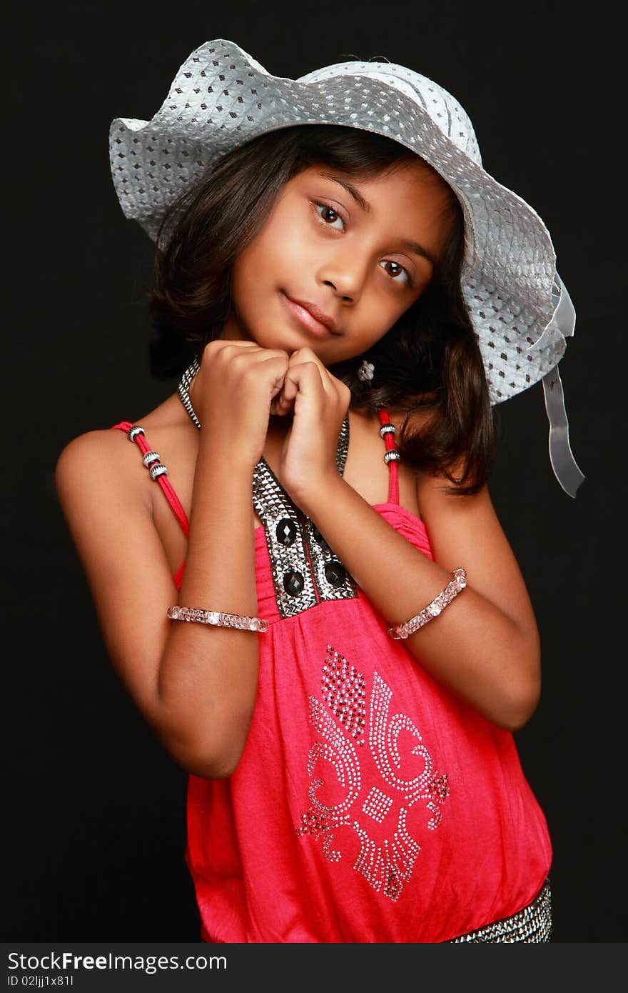 An Indian girl child posing with a smile wearing a white hat and red dress. Black background. An Indian girl child posing with a smile wearing a white hat and red dress. Black background