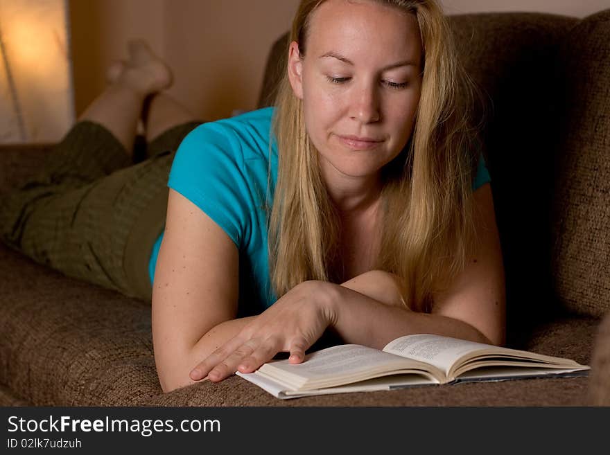 Blond girl (young woman) reading a book, lying on a sofa in a romantic mood, smiling. Blond girl (young woman) reading a book, lying on a sofa in a romantic mood, smiling