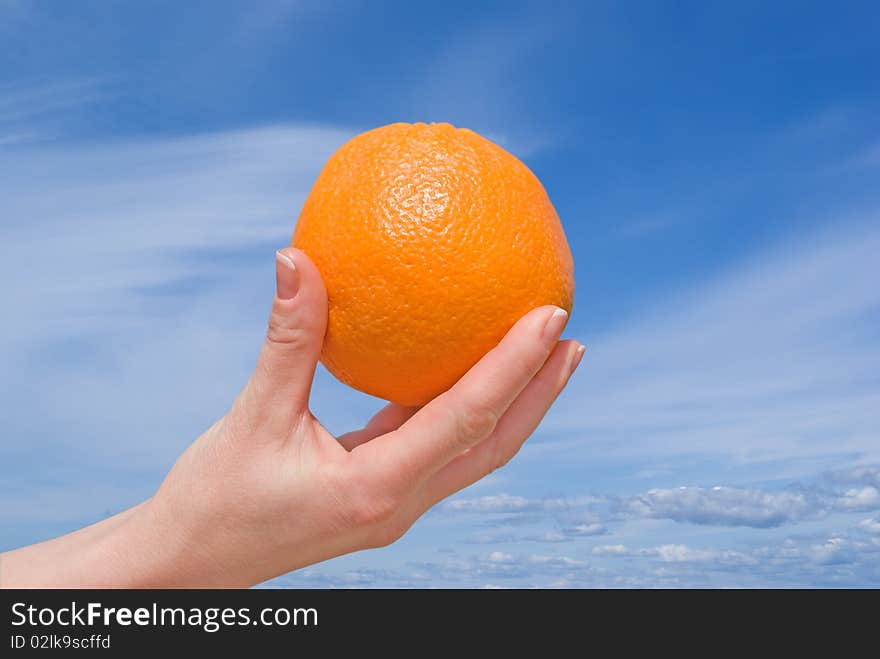 Hand with an orange against the sky