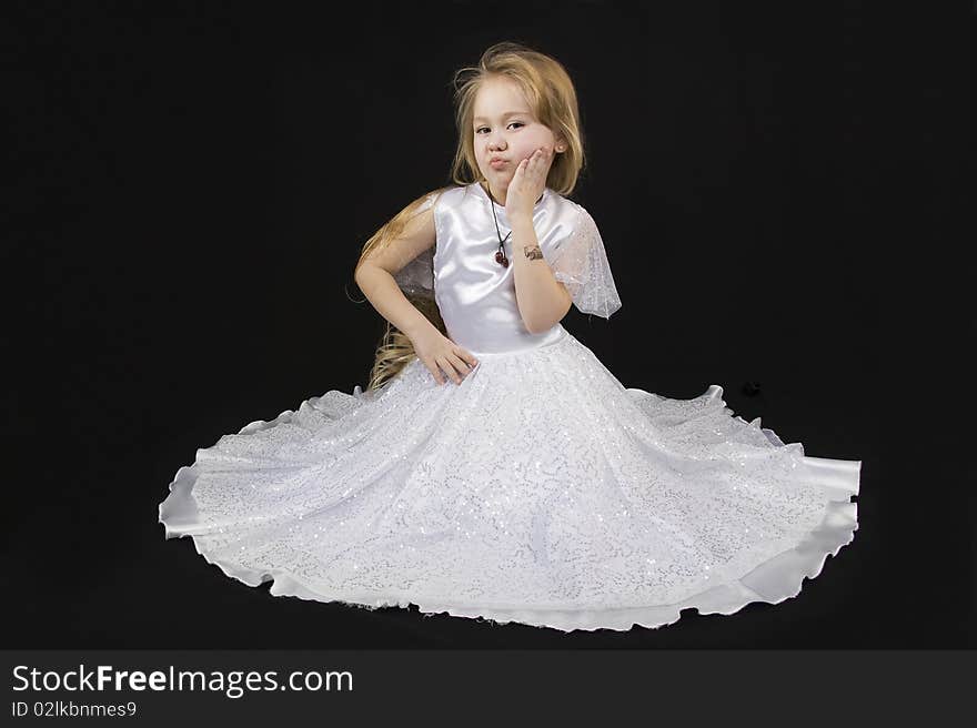 The girl the princess in a white dress sits opposite to a black background. The girl the princess in a white dress sits opposite to a black background