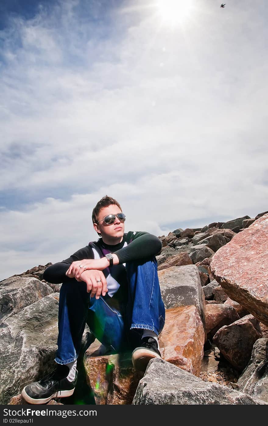 Young man on the rocks on clouds background in the eyeglasses