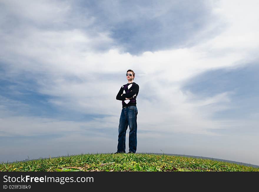 Young man in the clouds on the green grass in the eyeglasses