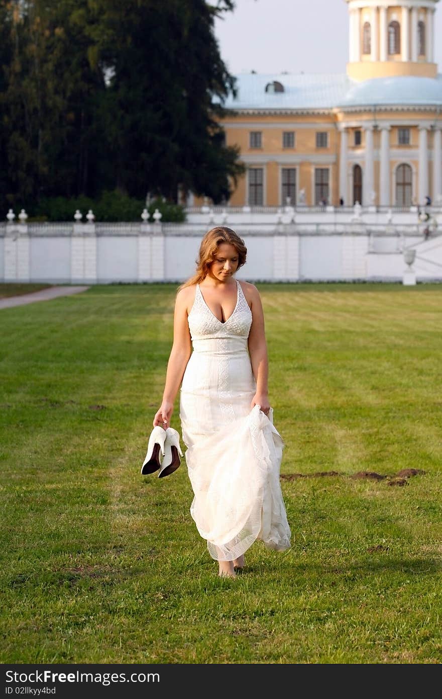 The girl with shoes in hands going on a grass.