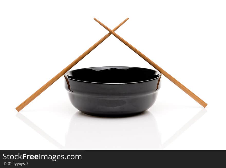 Crossed chopsticks on a black bowl on white