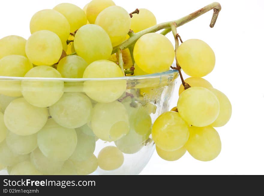 Close and low level angle capturing a glass bowl of grapes arranged over white. Close and low level angle capturing a glass bowl of grapes arranged over white.