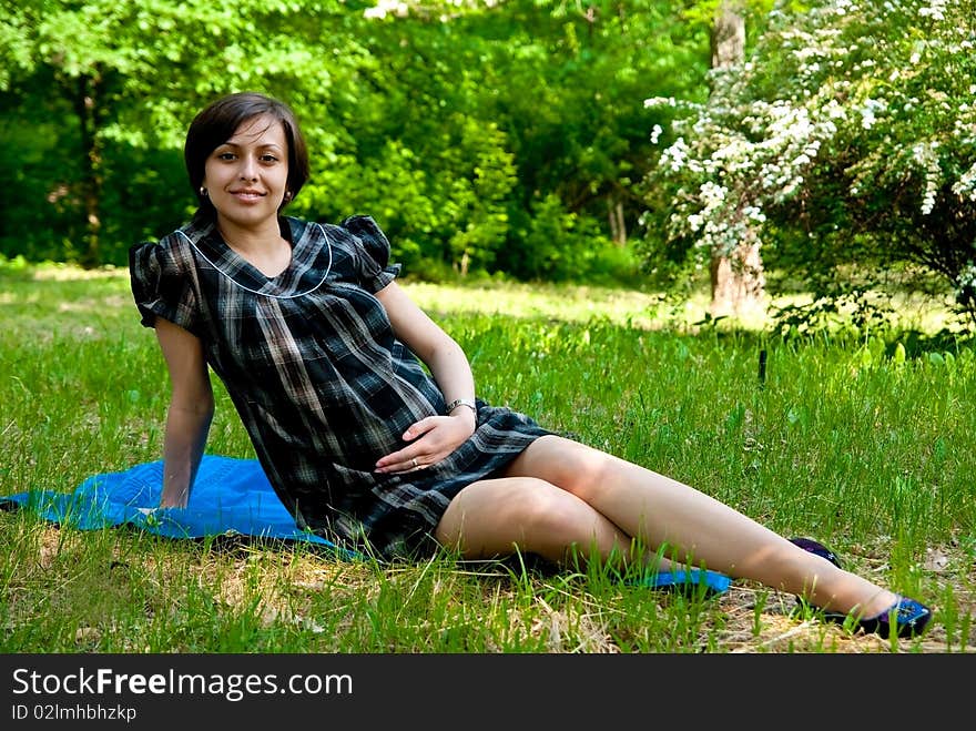 Beautiful smiling pregnant woman relaxing on grass in park.