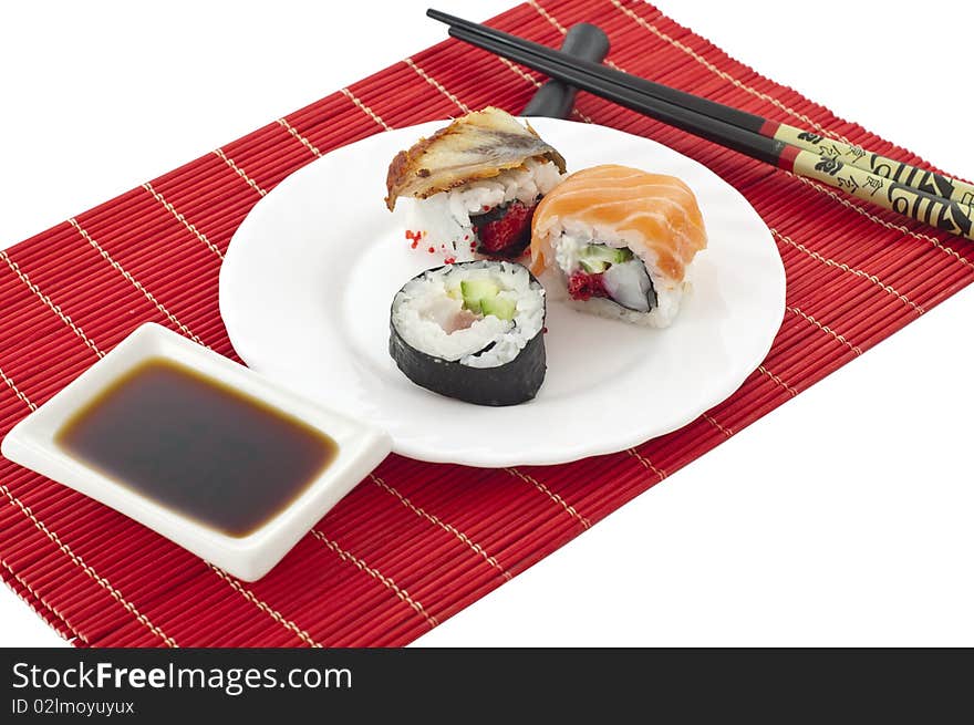 The Sushi, the chopsticks, soya sauce on a red bamboo mat on a white background. The Sushi, the chopsticks, soya sauce on a red bamboo mat on a white background