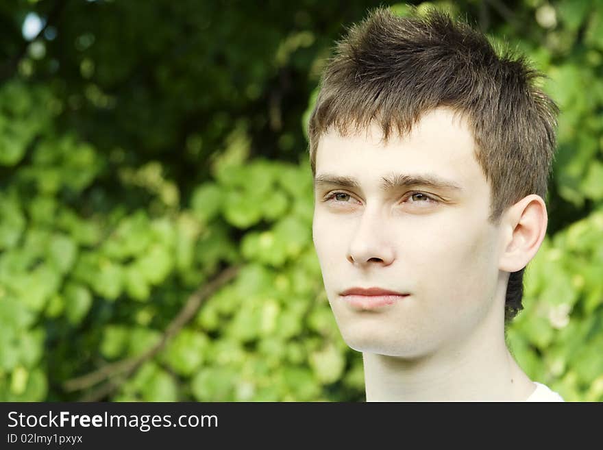 Teenager in a park in a white shirt against the green leaves of the tree. Teenager in a park in a white shirt against the green leaves of the tree