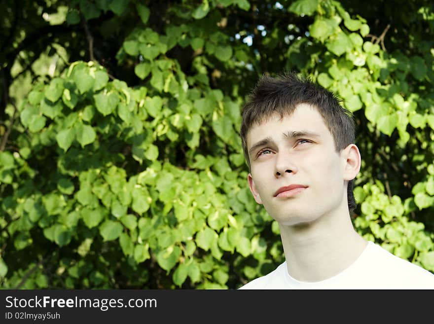 Teenager in a park in a white shirt against the green leaves of the tree. Teenager in a park in a white shirt against the green leaves of the tree