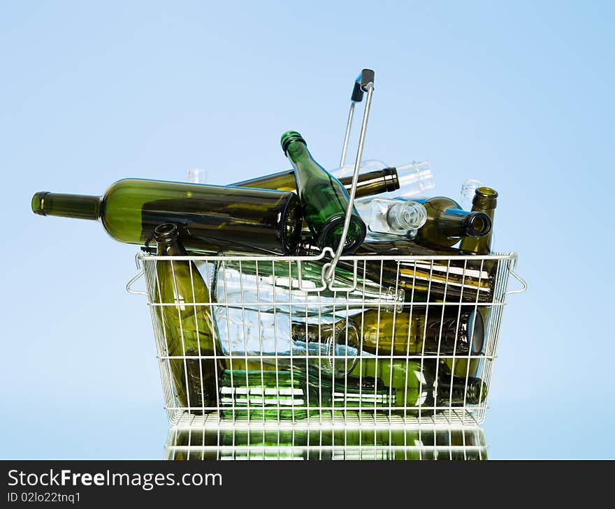 Empty glass bottles in a wastebasket on blue background