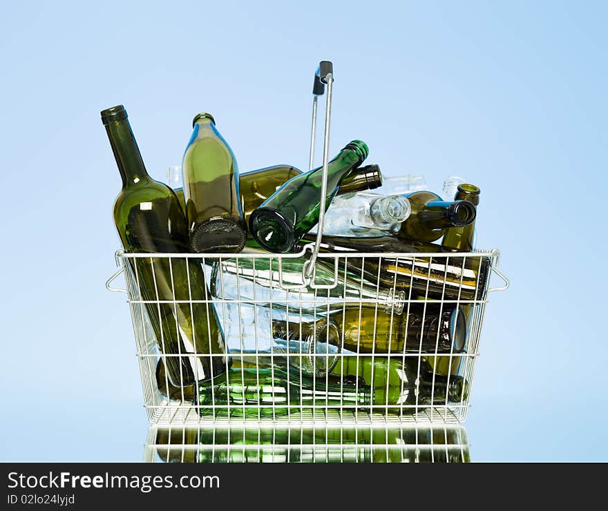 Empty glass bottles in a wastebasket on blue background