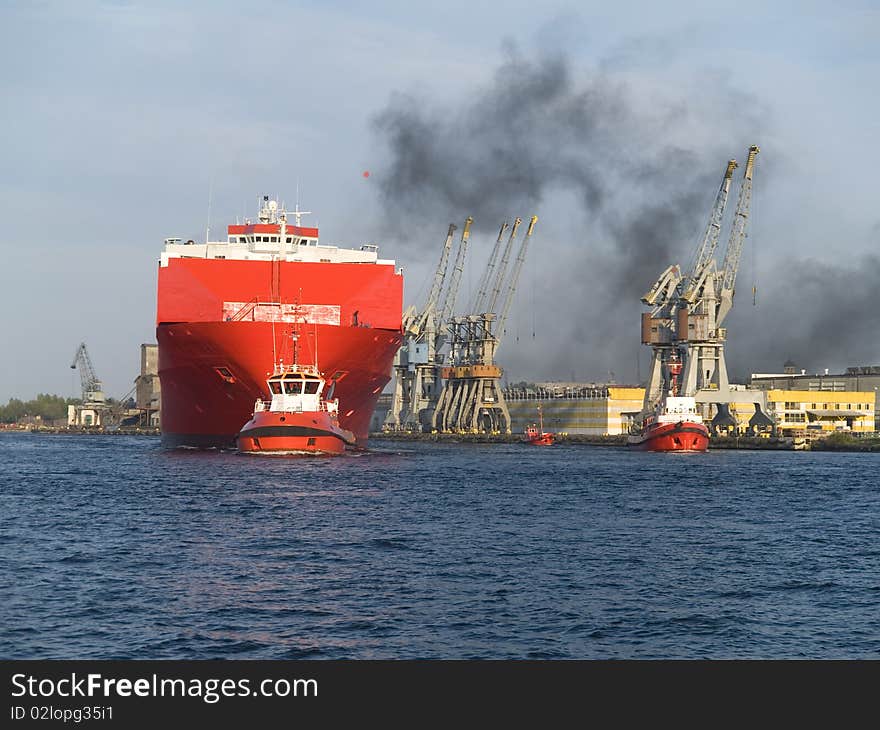 A huge ship leaving a habour with assistance of tugboat