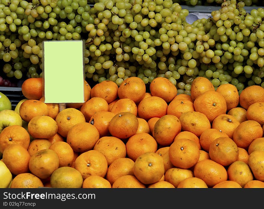 Green grapes and oranges with a sign at a market. Green grapes and oranges with a sign at a market