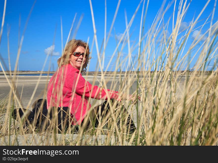 Woman sitting in the sand dunes on the beach with blue sky