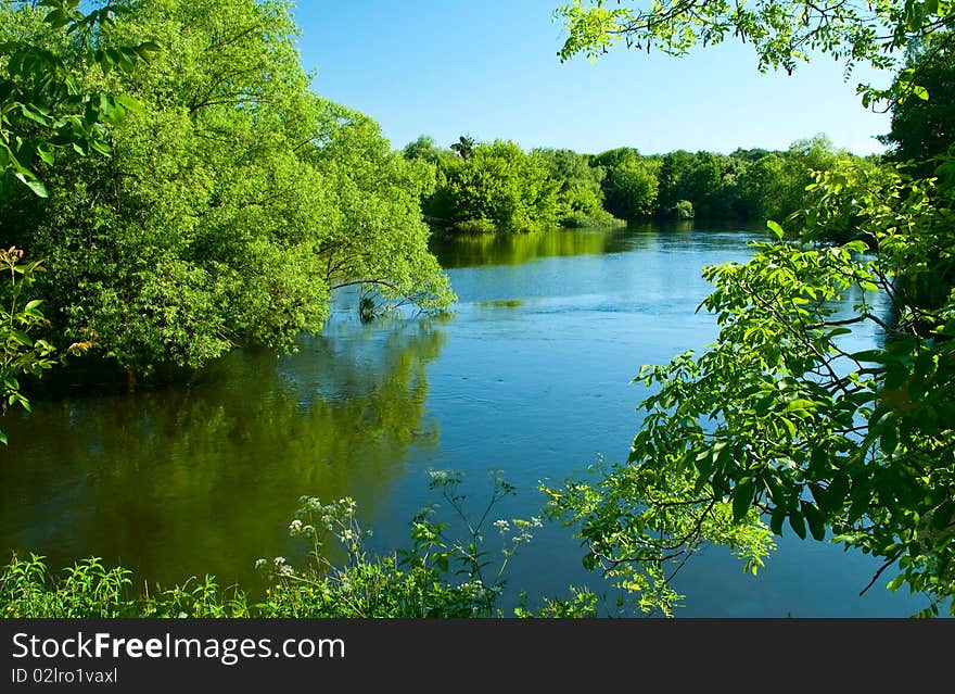 Shows the river, trees, grass and sky.