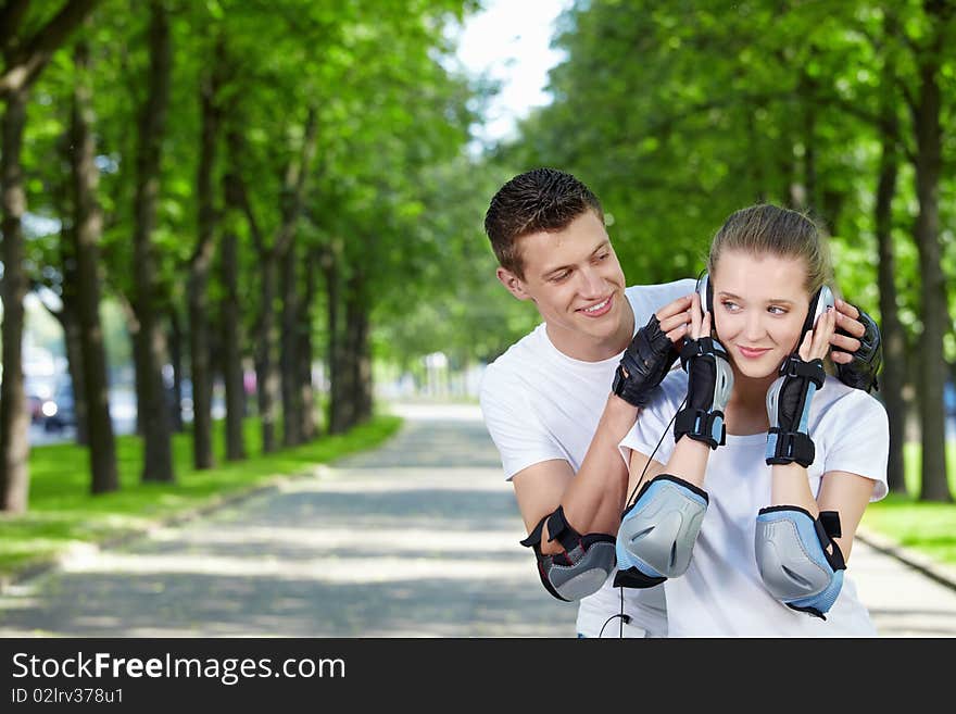 The young man looks at the girl listening to music in ear-phones in park