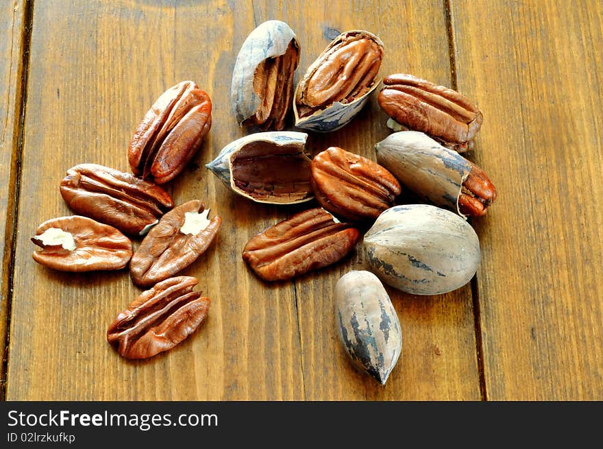 Pecans, whole and broken lie on the background of a wooden table. Pecans, whole and broken lie on the background of a wooden table