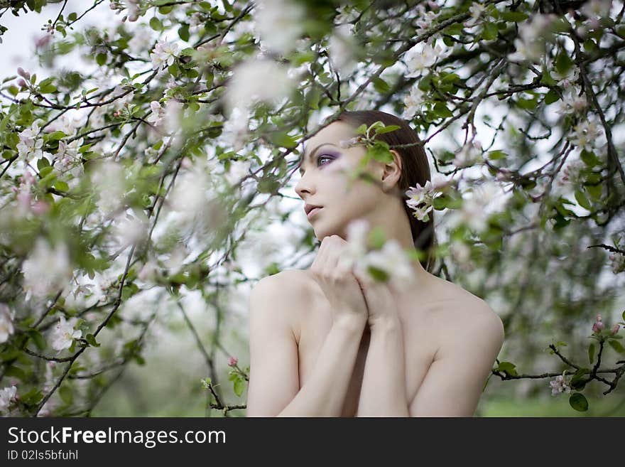 Young nude girl near blooming apple tree