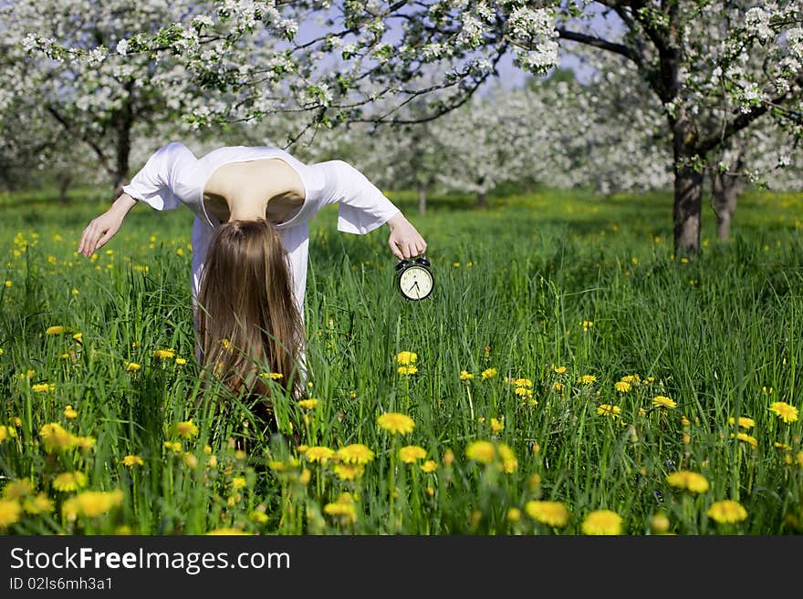 Young Girl With An Alarm Clock Near Blooming Apple