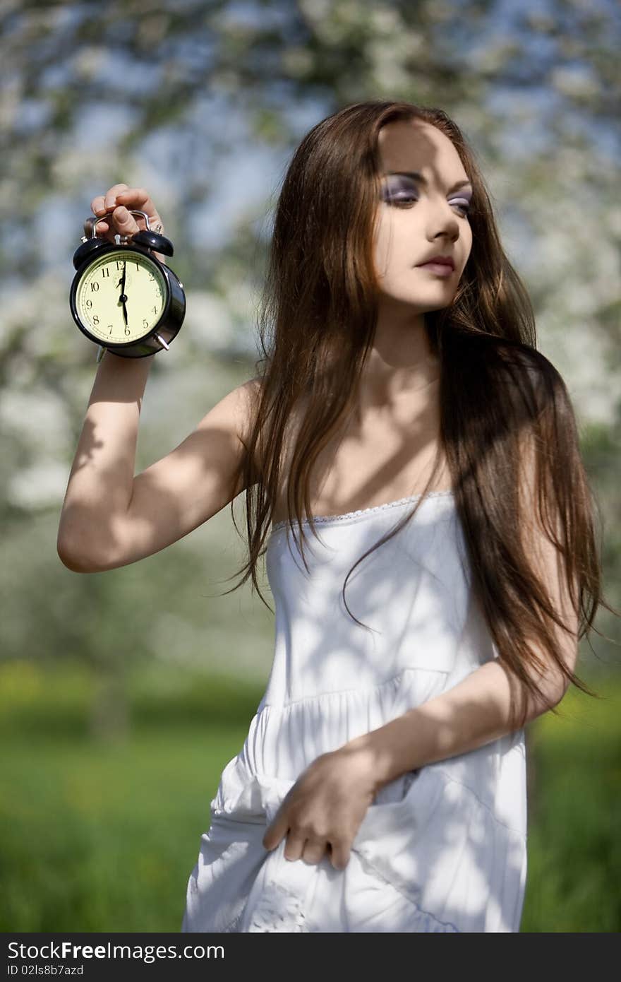 Young girl in a white dress with an alarm clock in the hands in the meadow. Young girl in a white dress with an alarm clock in the hands in the meadow