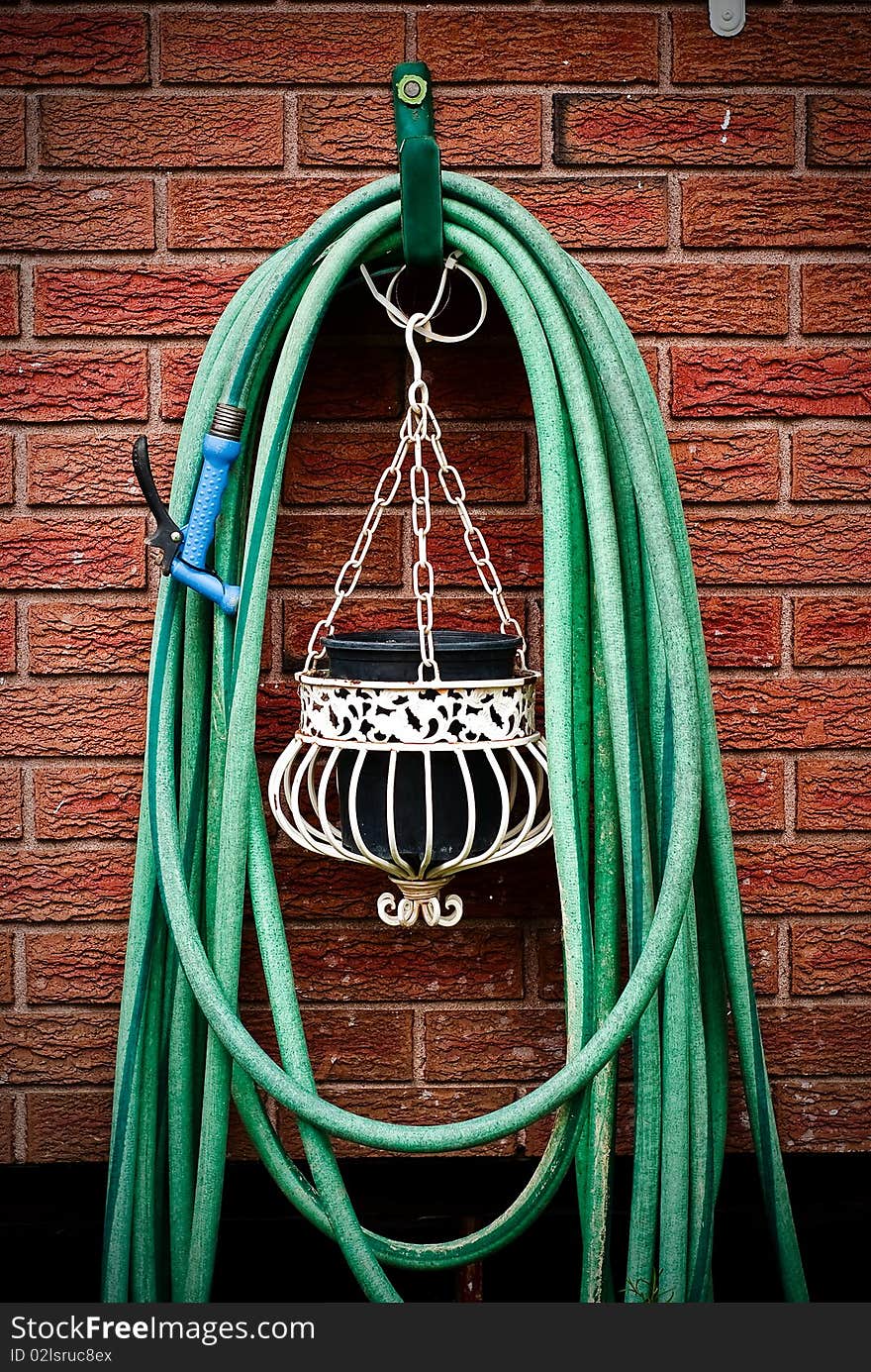 A common home garden hose coiled up and hanging on brick wall with hanging planter underneath. A common home garden hose coiled up and hanging on brick wall with hanging planter underneath.