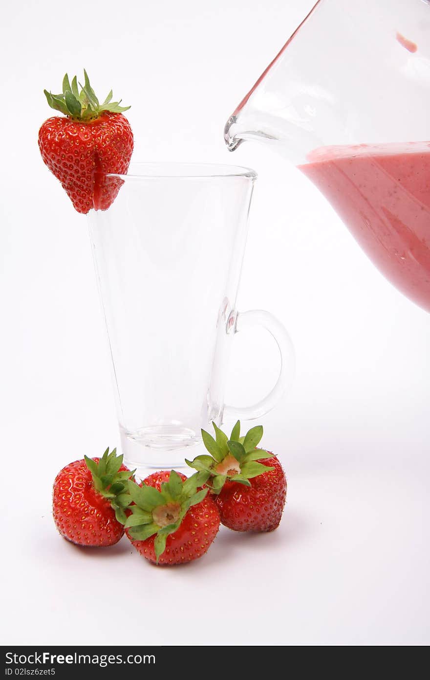 Strawberry shake being poured into a glass from a jug and some strawberries on white background