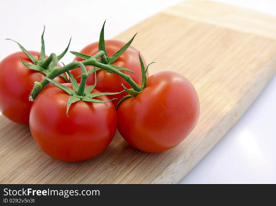 Four Red Tomatoes on a Wooden Cutting Board.